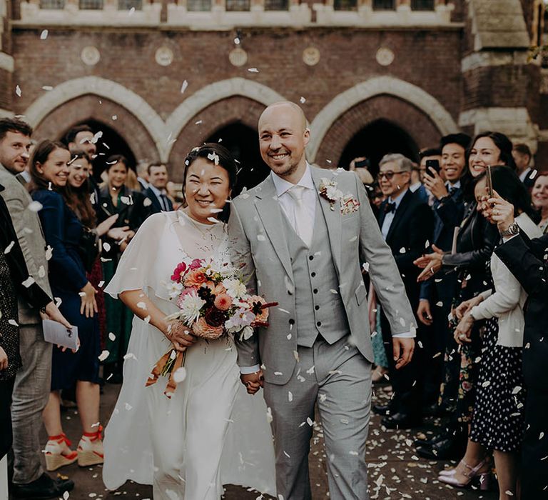 Bride & groom walk through confetti as bride wears wedding dress sample complete with cape  | Irene Yap Photography