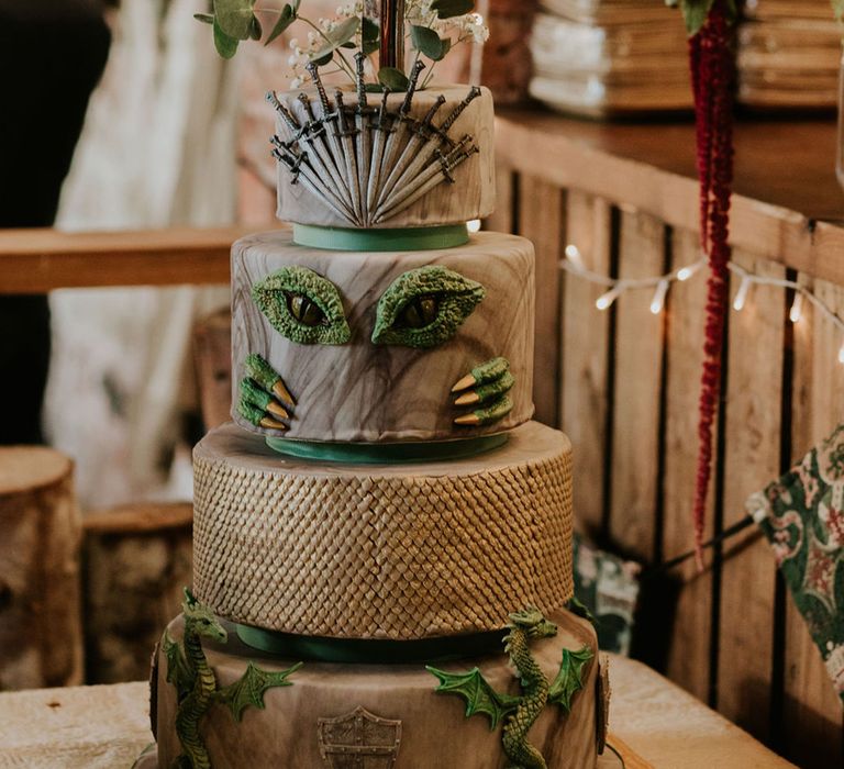 Themed four tier wedding cake with swords, dragons, scales and green borders with sword in the cake to be pulled out by bride and groom medieval fantasy wedding