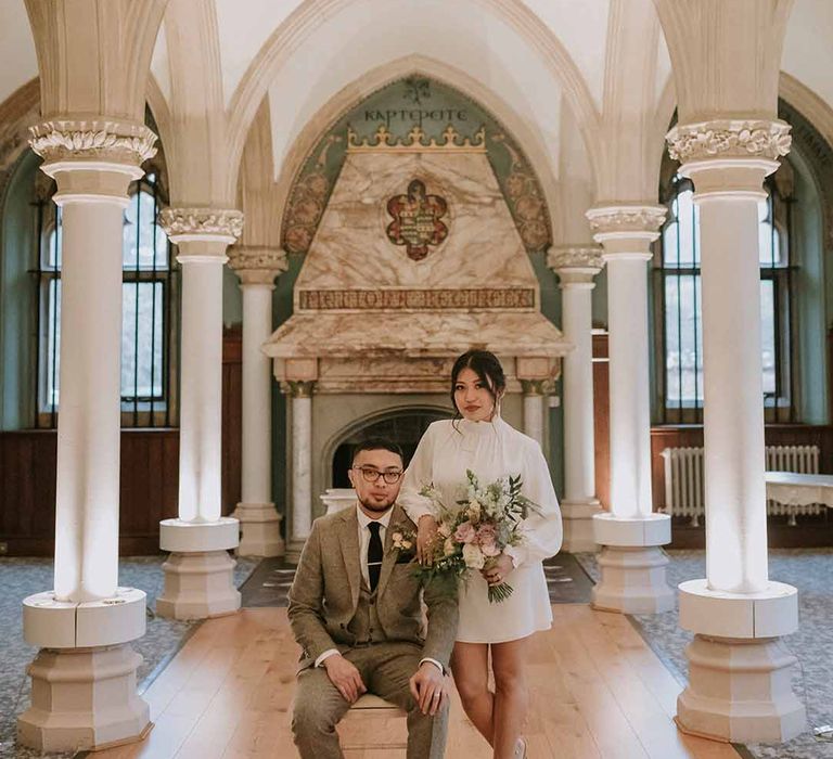 Groom in Tru Clothing suit and GH Bass x Maharishi, bride in Vanessa Cocchiaro Paris short wedding dress and Jimmy Choos with neutral floral bouquet 