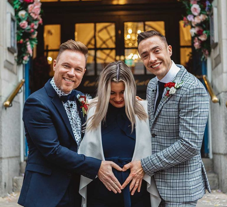 Grooms place their hands in a heart shape on surrogates belly