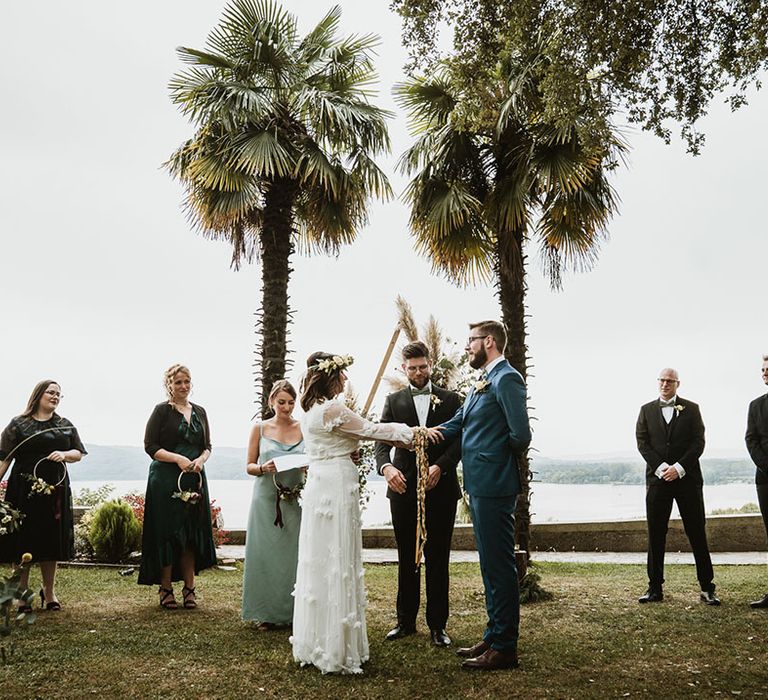 Coastal handfasting ceremony with bride in a long sleeve wedding dress and groom in a blue suit