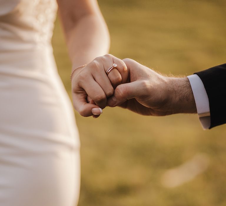 Rose gold engagement ring and wedding band on bride's hand as groom holds her hand