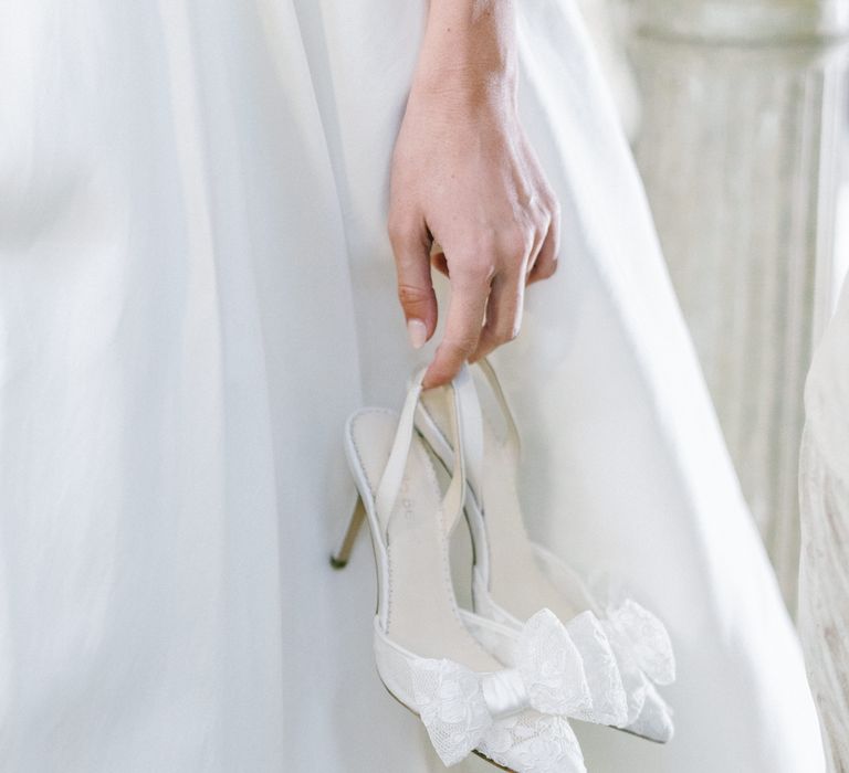 Bride in white dress holding the sheer lace wedding court shoes with bow