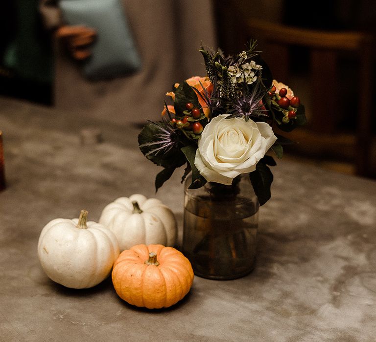 White and orange pumpkin decor with small arrangement of white and orange flowers for autumnal wedding