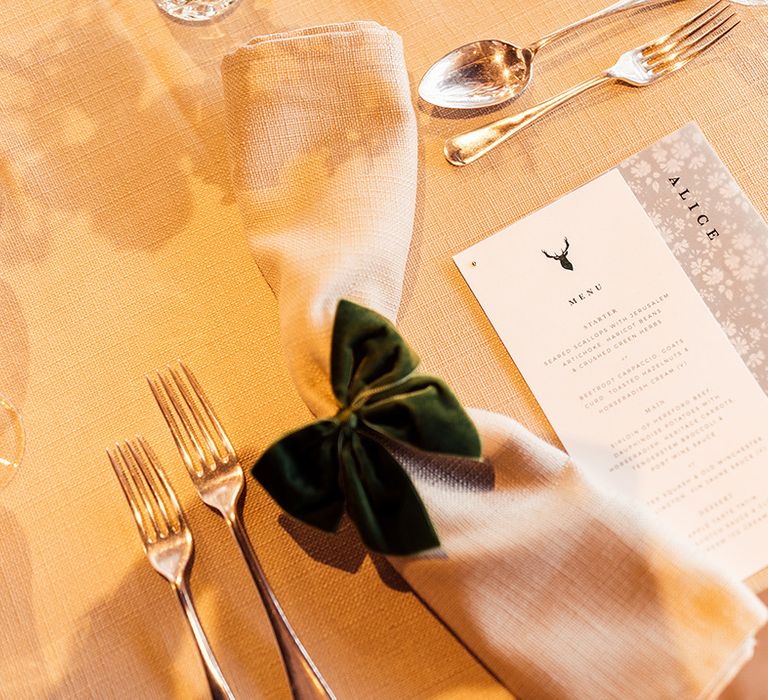 Cream napkin with velvet green bow with menu card decorated with stag emblem and floral name place card 