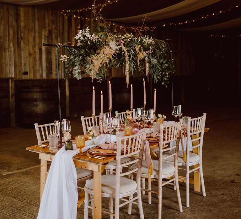 Rustic barn wedding venue with ceiling drapes and fairyliphts and tablescape with floral installation and coloured candles 