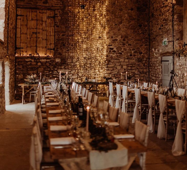 Rustic Eden Barn wedding venue with fairy lights, white tablecloth banquet tables, white wedding drape chair back decor 