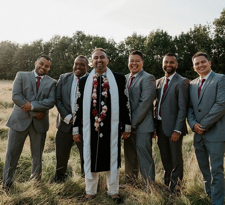 Groom stands with his groomsmen who wear grey suits and red ties