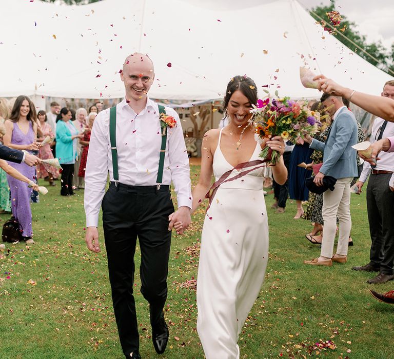 Bride & groom walk through confetti petals dried from garden after wedding ceremony 