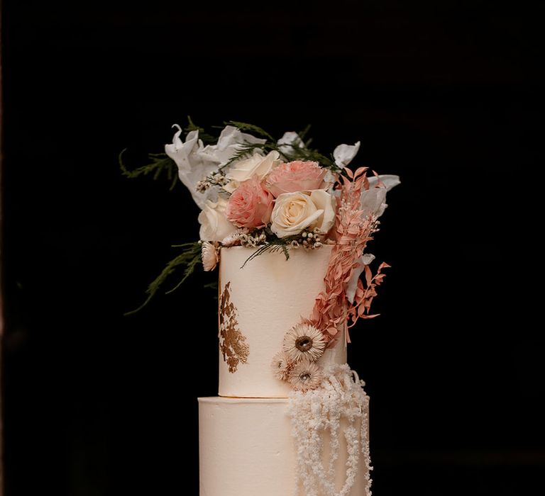 three-tier buttercream wedding cake with gold detail and drip design topped with fresh pink flowers 