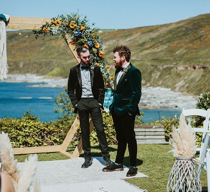 Groom wears green velvet suit jacket and stands beside groomsmen who wears black velvet dinner jacket 