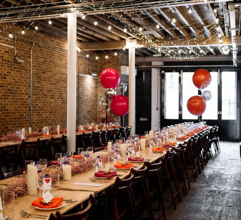 Wooden banquet tables complete with orange and pink wedding theme alongside large balloons and fairy lights at the 100 Barrington