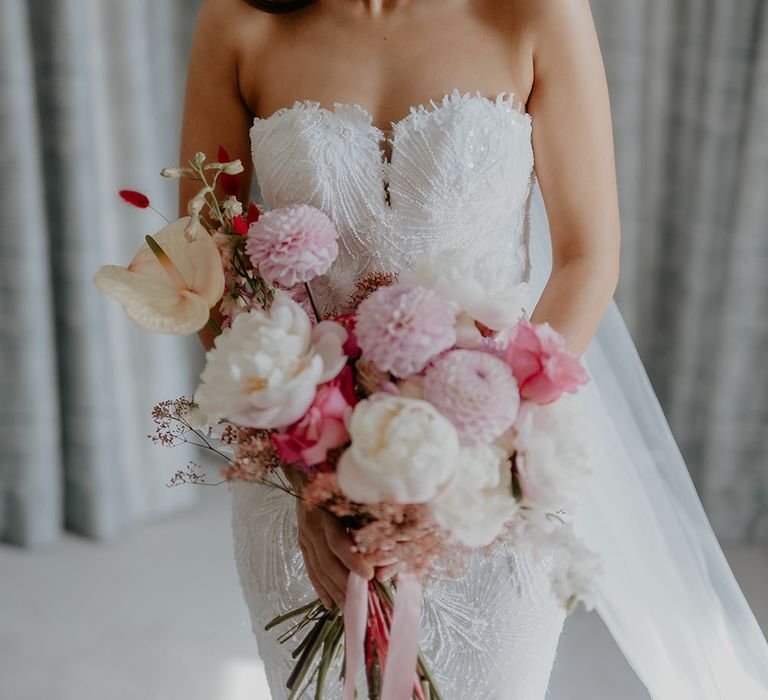 Bride wears strapless Pronovias fitted wedding dress with lace embellishment and holds white and pink floral bouquet