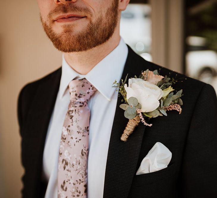 Groom wears floral styled tie and white rose buttonhole tied with brown string 