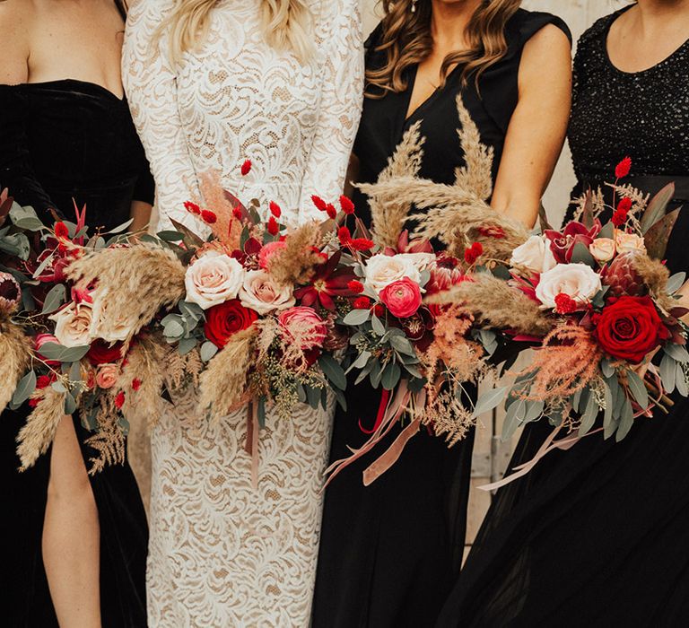 Bridal party with different styles of black dresses all holding pink and red bouquets