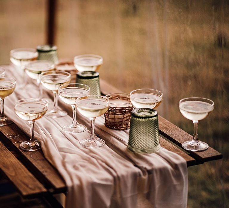 Wooden table with white table runner, coloured glassware and cocktails for guests 