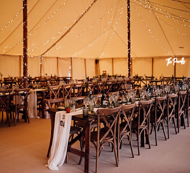 Marquee wedding with fairy lights, custom neon sign and banquet tables with white runners and green decor 