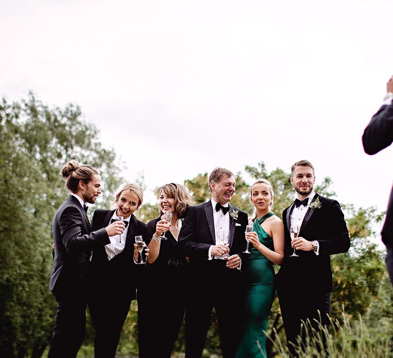 Groom stands with wedding party with bridesmaid in suit and black-tie dress code