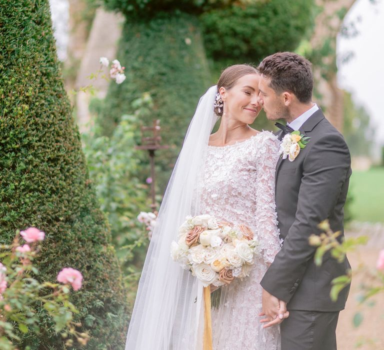 The bride in a long sleeve lace flower appliqué wedding dress leans back into the groom wearing a black tie 