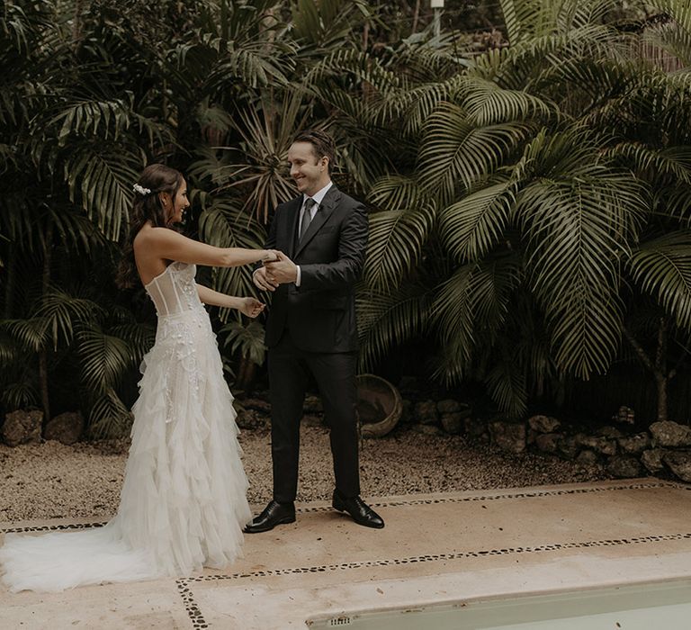 Bride wears corset styled fitted wedding dress with ruffled skirt as her groom sees her during first look moment 