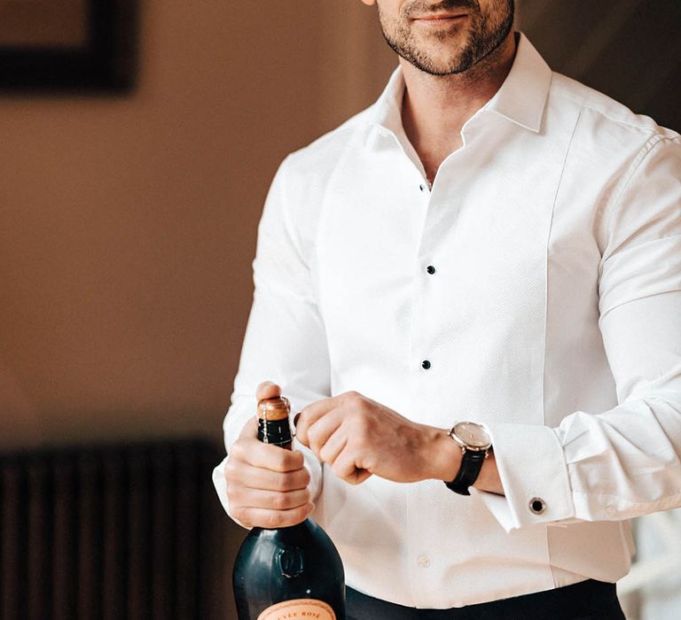 The groom opens a bottle of alcohol on the morning of the wedding as he gets ready 