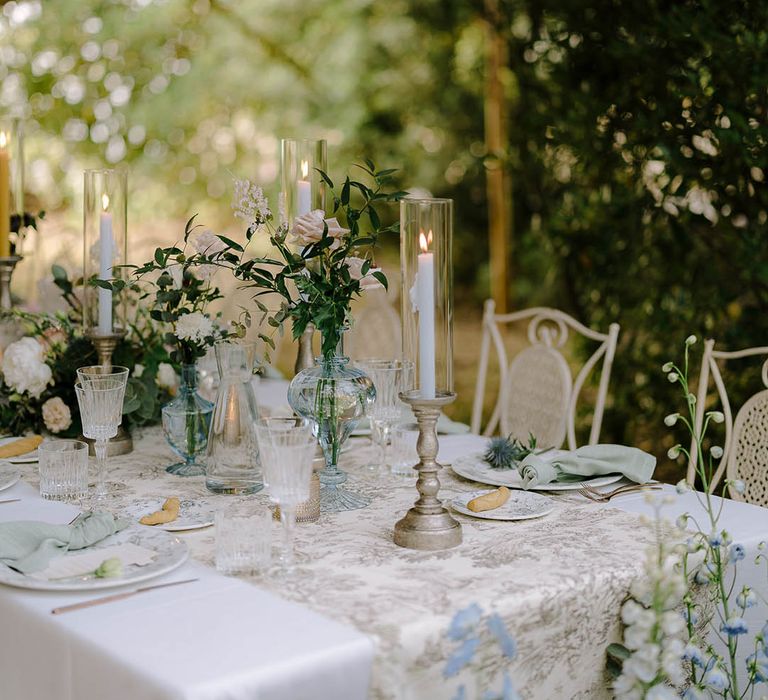 Beautiful Italian tablescape with ribbed glassware, gold candlestick holders and flower arrangements that include thistles, peonies, carnations and wildflowers