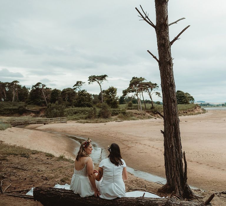 Brides sit sharing an intimate moment together as they talk to each other on a log 