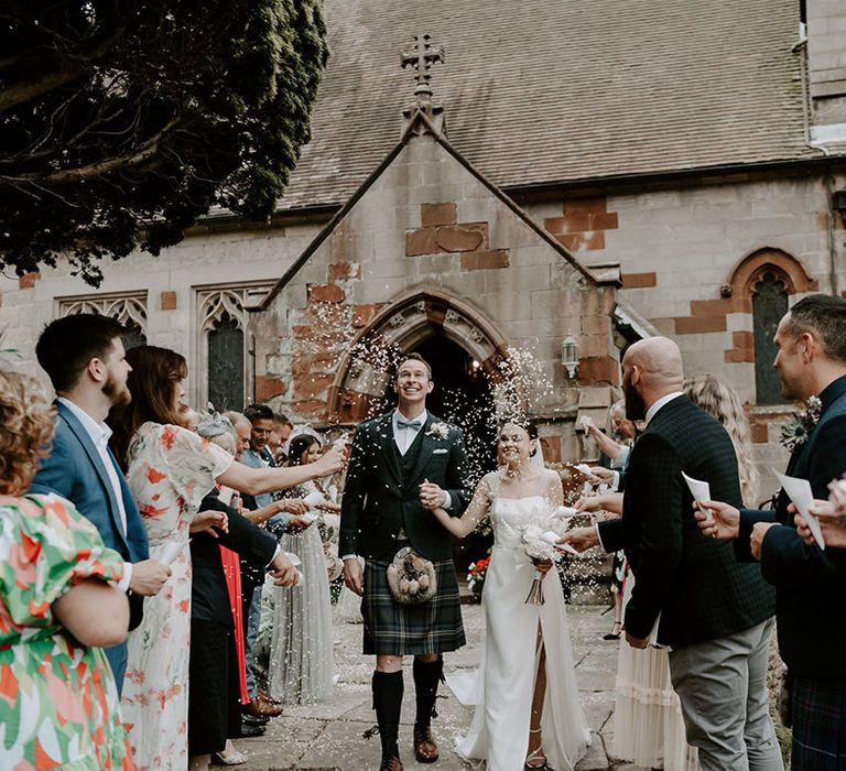 Bride and groom exit their ceremony smiling as a married couple to white confetti 