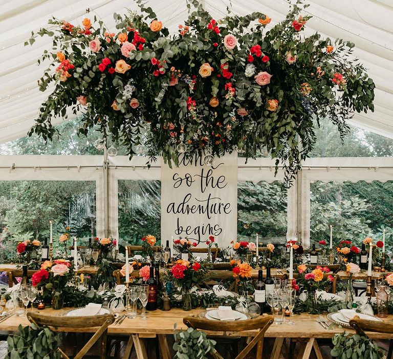 Marquee wedding with white wedding signage and red and orange rose flower cloud 