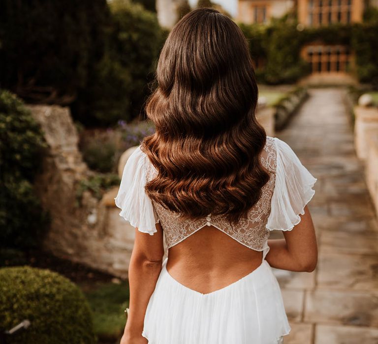 Bride in satin open back wedding dress with button details and butterfly sleeves, ruffled and layer on the back