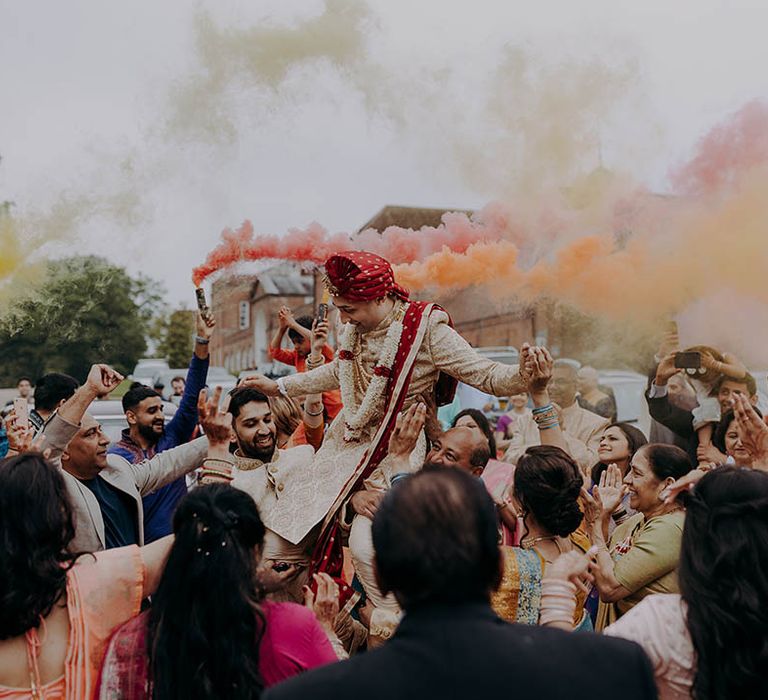 Wedding guests lift groom as they surrounded him whilst carrying colourful smoke bombs