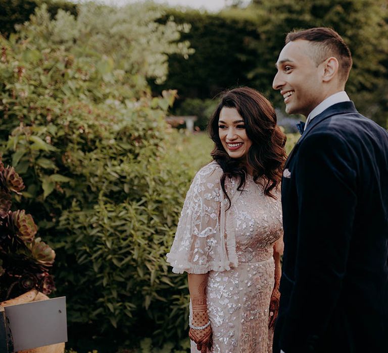 Bride wears her black hair in loose curls and stands beside her groom in blue velvet suit 