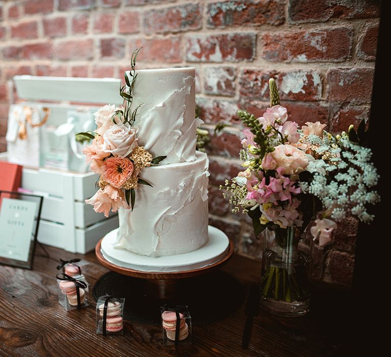 Two tiered buttercream wedding cake with icing details and light pink rose, foliage and golden decorations 