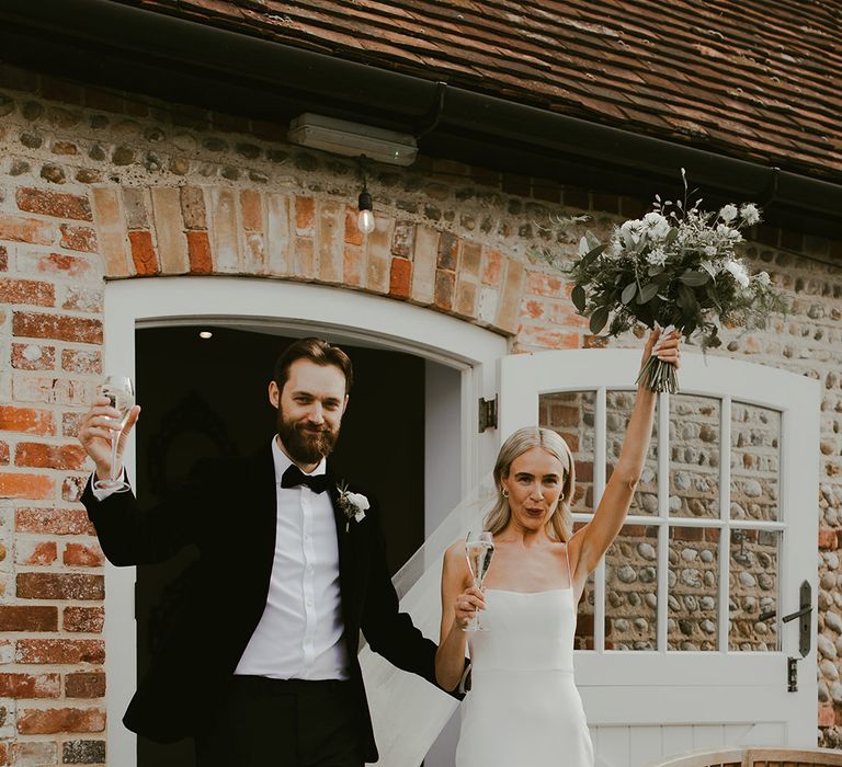 Bride exits the ceremony in a fitted wedding gown with small gold hoops holding a classic green and white bouquet with the groom in black tie 