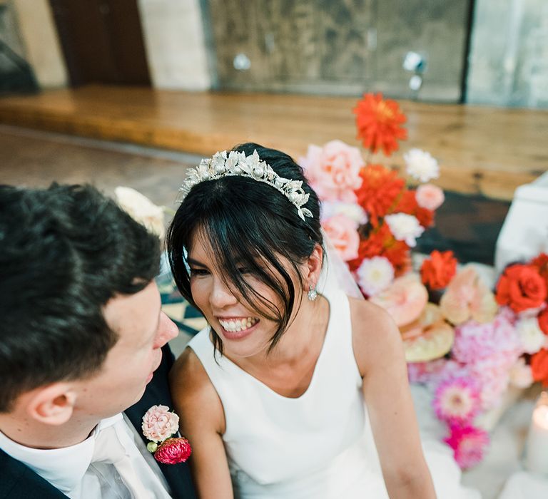 East Asian bride wears feather embellished bridal crown in her black hair and looks lovingly toward her groom