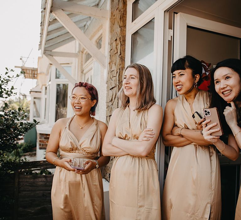 Bridesmaids wear gold bridesmaid dresses as they watch groomsmen play traditional door games 