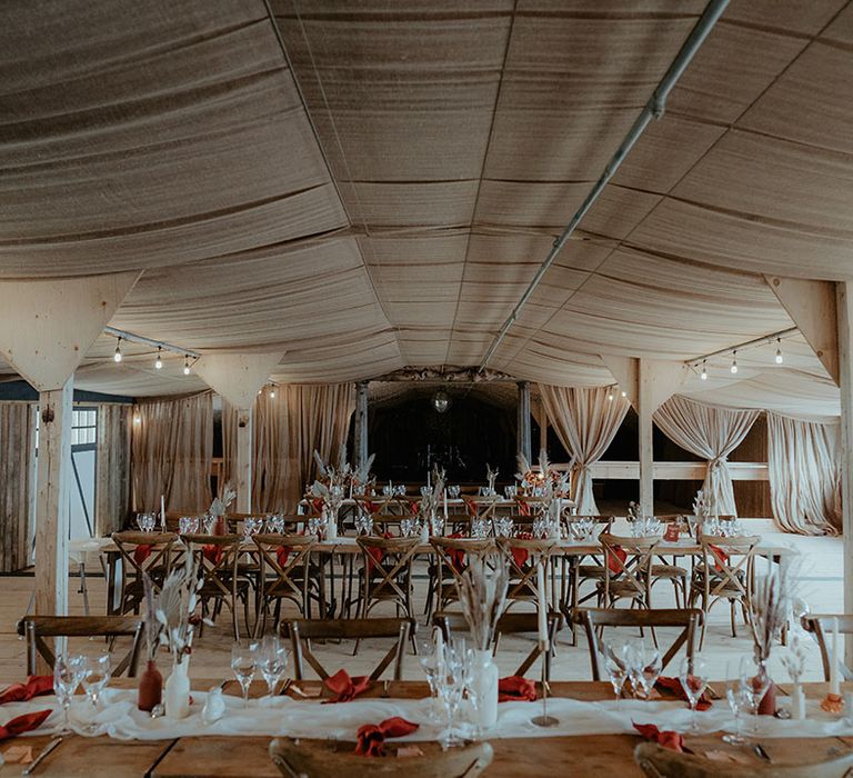 Rustic glam Rhyse Farm wedding venue with wooden tables with white table runners, orange napkins and bunny grass floral arrangements 