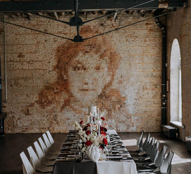 Contemporary monochrome wedding tablescape with black red and white wedding decor - red and white roses, carnations and chrysanthemums, black and white tapered candles in clear candlestick holders, small black statues and three tier white wedding cake with black paint splatter icing 