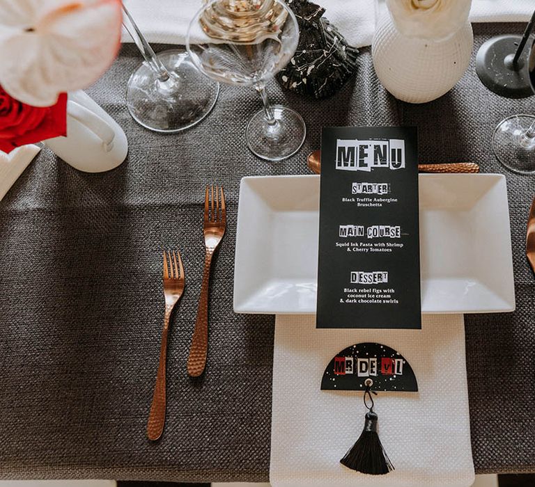 Edgy, contemporary black wedding stationery on square white plate and black red and white wedding table name with black tassel accessory 