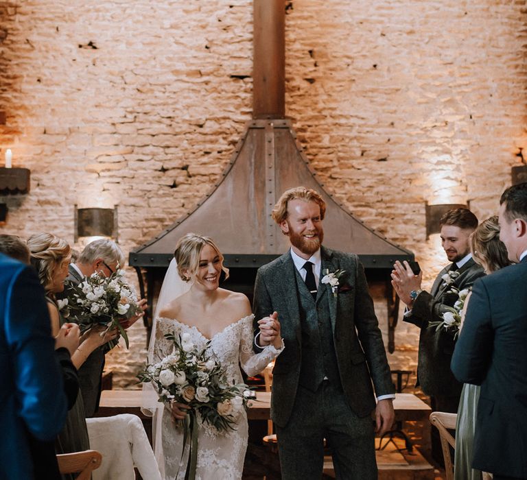 Rustic barn wedding with the bride in a classic lace wedding dress with the groom in a three piece grey tweed suit 