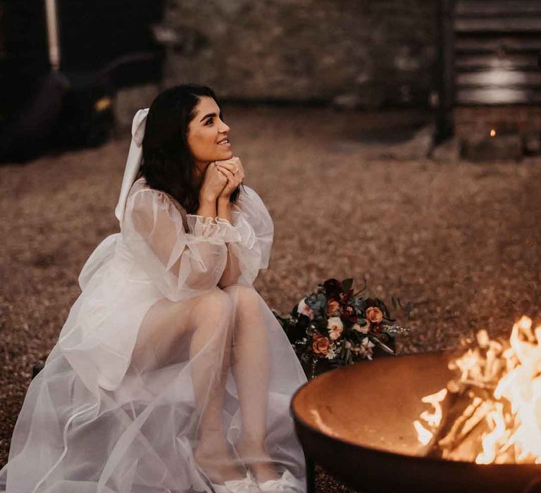 Bride in sheer overlay puff sleeve wedding dress and strapless wedding heels sitting by the fire pit 