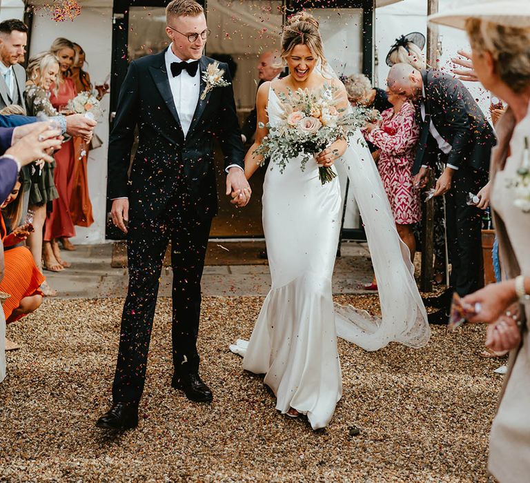 Fun confetti moment for the bride and groom after their civil wedding ceremony at their rustic luxe wedding in Suffolk