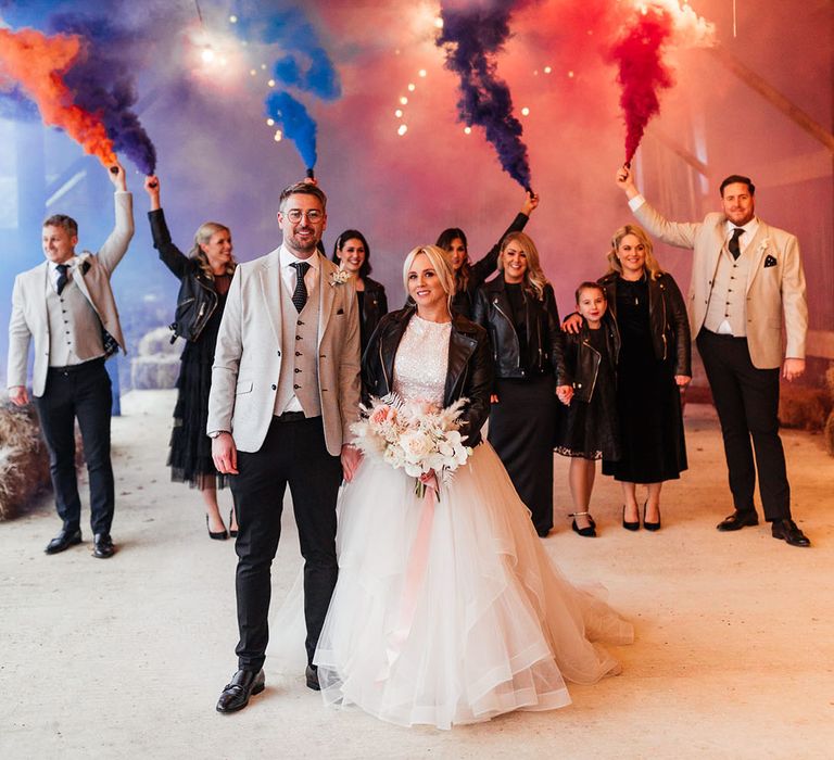 Smoke bomb portrait of the bridesmaids in black bridesmaid dresses, groomsmen and groom in matching light greys suits and the bride in sparkly bridal separates