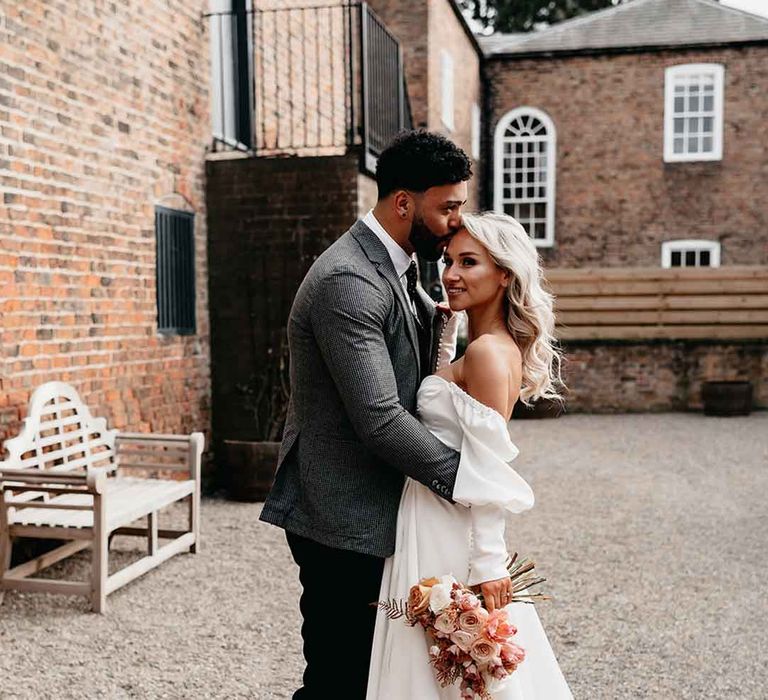 Bride in off the shoulder long sleeve wedding dress with slight cowl neck slit standing with groom at Lodge Farm wedding venue 