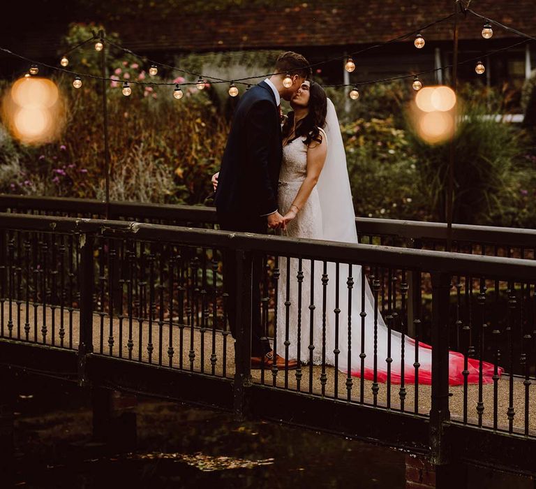 Bride wearing sleeveless lace wedding dress and church length red ombre veil kissing groom in deep blue suit at The Orangery Maidstone