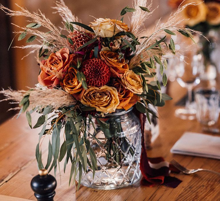 Orange and red roses and dahlias with pampas grass in glass vases decorating the wedding tables