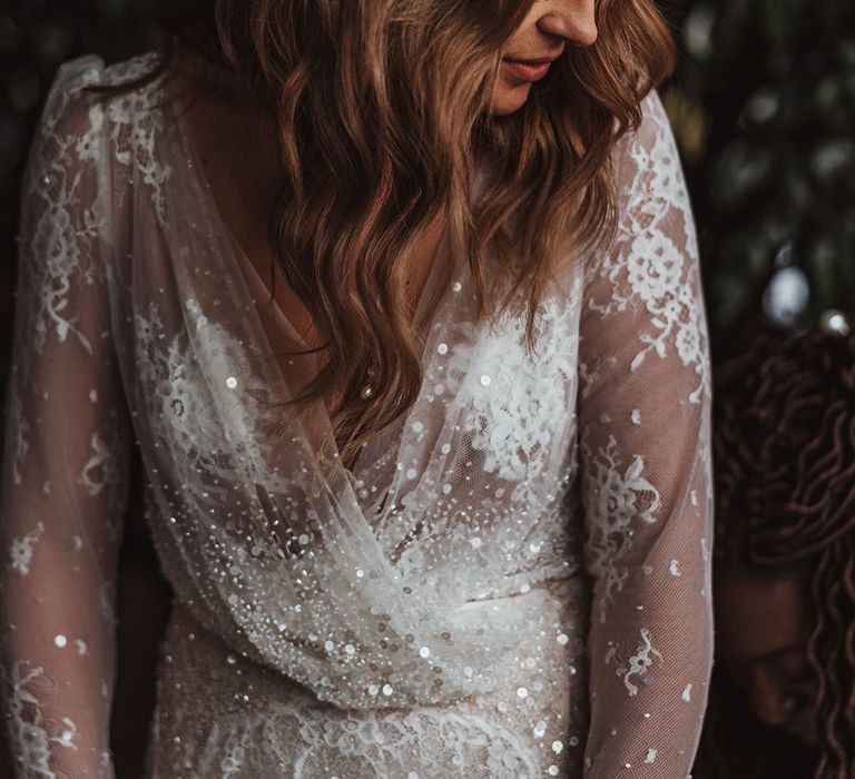 Bride in sheer long sleeve winter wedding dress with lace details and sequins with curled brown hair 