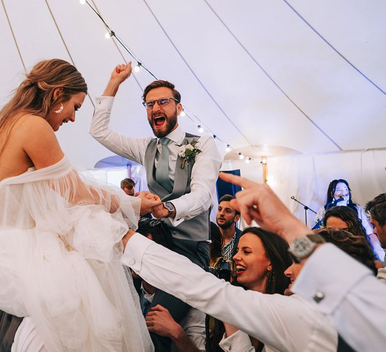 The bride and groom are lifted up by their wedding guests as they party for the wedding reception 