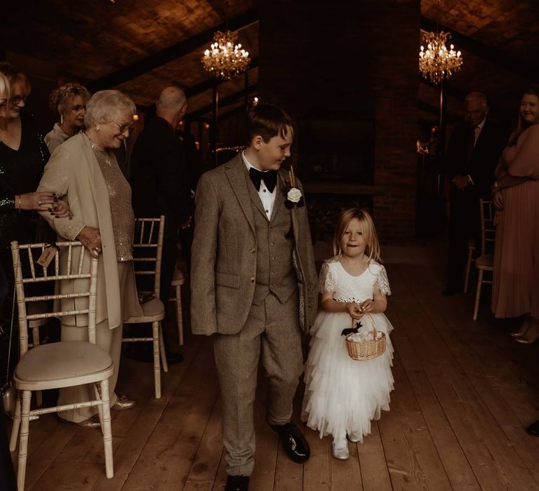 Groomsman in three piece grey textured suit and black bowtie walking down the aisle with flower girl in short sleeve tulle layered flower girl dress 