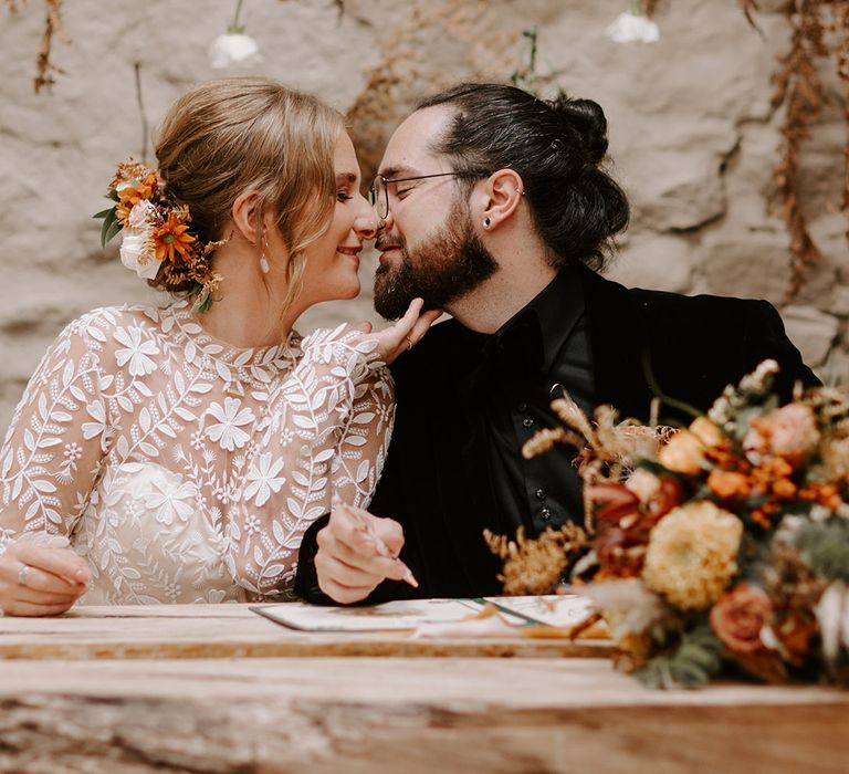 Bride in long sleeve boho wedding dress kisses the groom in all black velvet suit as they sign the register 